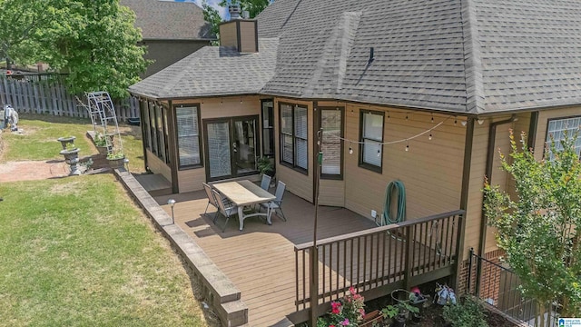 rear view of property featuring roof with shingles, a lawn, a wooden deck, fence, and outdoor dining space