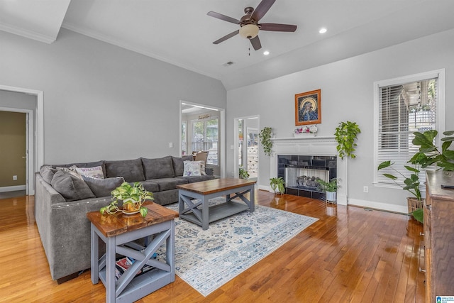 living room with ceiling fan, crown molding, a tile fireplace, baseboards, and hardwood / wood-style floors