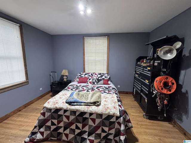 bedroom featuring baseboards, light wood finished floors, and multiple windows