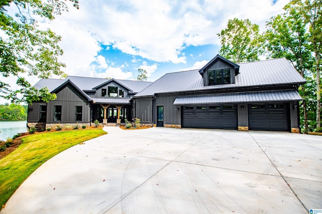 modern farmhouse with stone siding, a garage, a front yard, driveway, and metal roof