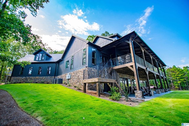 rear view of house featuring board and batten siding, a patio area, a yard, and stone siding