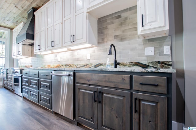 kitchen featuring wall chimney range hood, decorative backsplash, dark wood-style flooring, stainless steel dishwasher, and white cabinetry