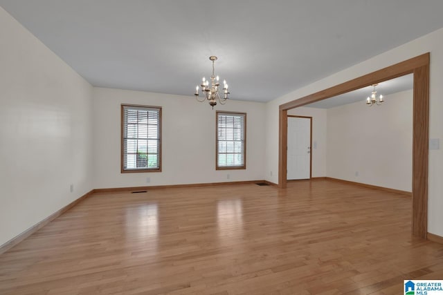 unfurnished room featuring light wood-type flooring, baseboards, and a notable chandelier
