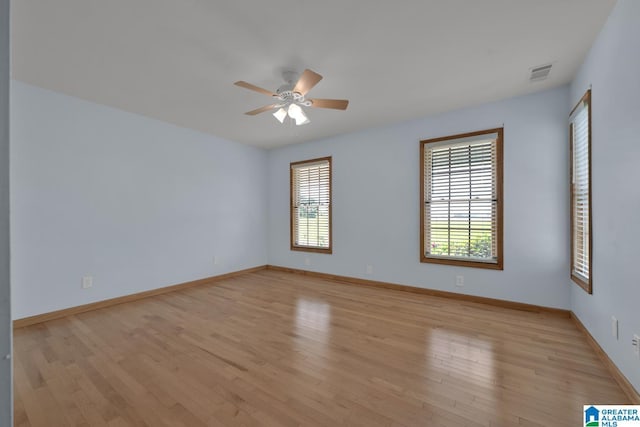 empty room featuring a wealth of natural light, a ceiling fan, light wood-style flooring, and visible vents