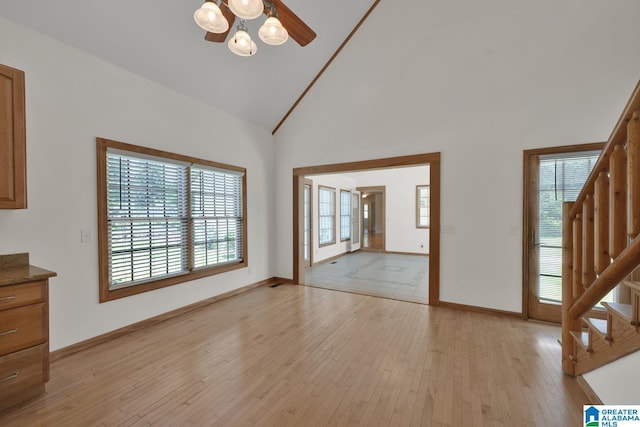 unfurnished living room with ceiling fan, stairway, high vaulted ceiling, baseboards, and light wood-style floors