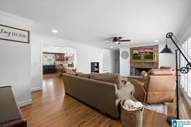 living area featuring a stone fireplace, wood finished floors, stairway, ceiling fan with notable chandelier, and ornamental molding