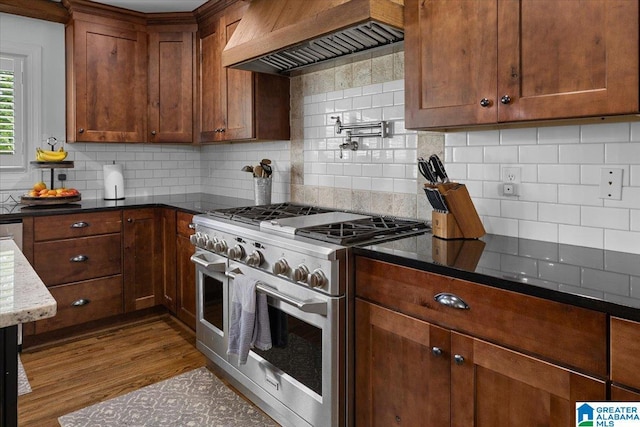 kitchen with decorative backsplash, double oven range, dark wood finished floors, custom exhaust hood, and dark stone counters