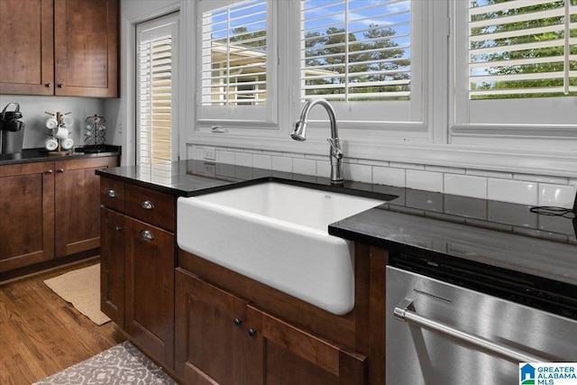 kitchen with stainless steel dishwasher, dark countertops, a sink, and wood finished floors