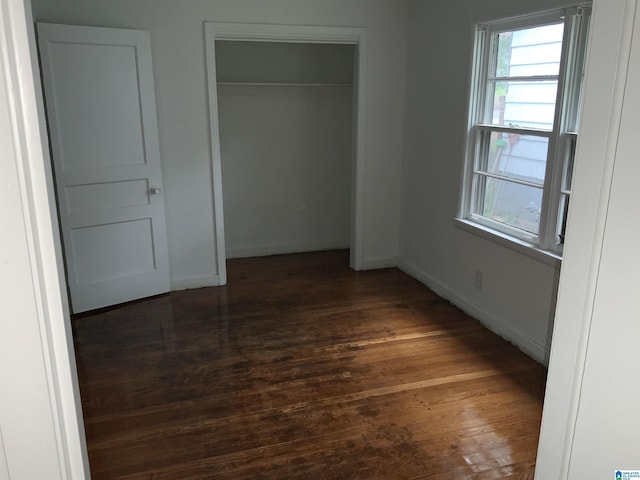 unfurnished bedroom with a closet, baseboards, and dark wood-style floors