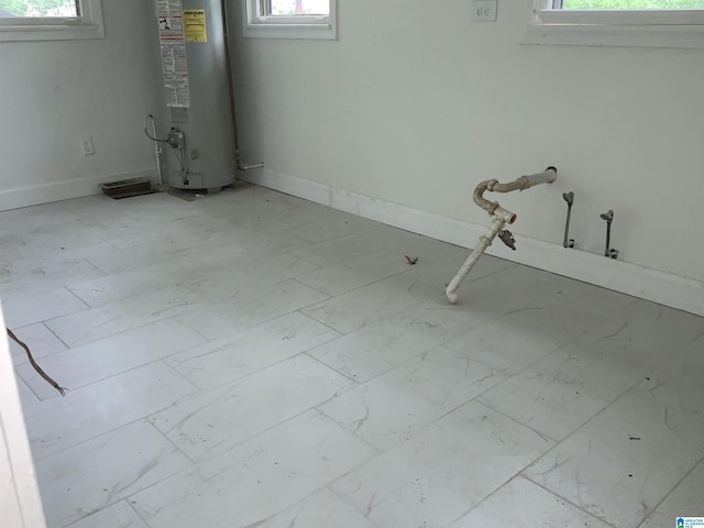 basement featuring baseboards, a healthy amount of sunlight, and water heater