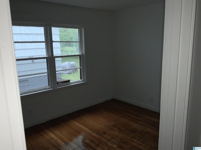empty room featuring plenty of natural light, dark wood finished floors, and baseboards