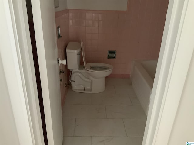 full bath with a bathing tub, toilet, tile walls, and marble finish floor