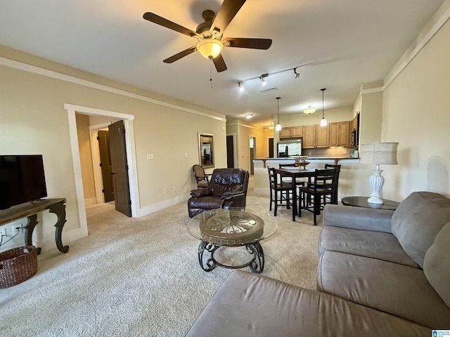 living room featuring rail lighting, light carpet, a ceiling fan, ornamental molding, and baseboards