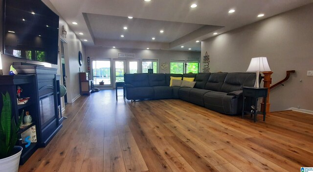 living area with a raised ceiling, a glass covered fireplace, hardwood / wood-style floors, recessed lighting, and baseboards