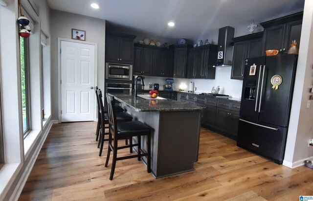kitchen featuring wall chimney range hood, a kitchen breakfast bar, stainless steel appliances, and a wealth of natural light