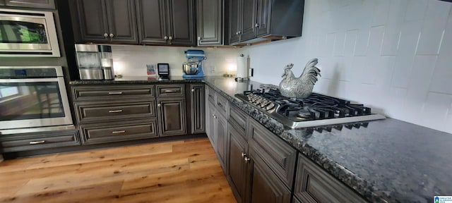kitchen featuring dark stone counters, appliances with stainless steel finishes, decorative backsplash, and light wood-style floors