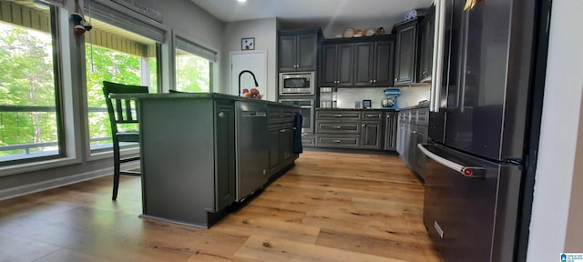 kitchen featuring appliances with stainless steel finishes, a wealth of natural light, dark countertops, and a center island with sink