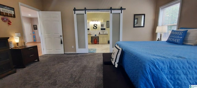 carpeted bedroom featuring baseboards, a barn door, and ensuite bath