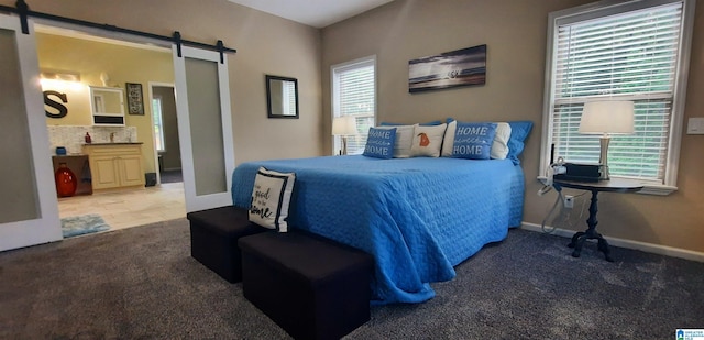 bedroom featuring carpet floors, a barn door, baseboards, and ensuite bath
