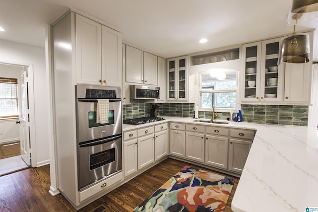 kitchen with stainless steel appliances, light stone countertops, dark wood-style floors, and a sink