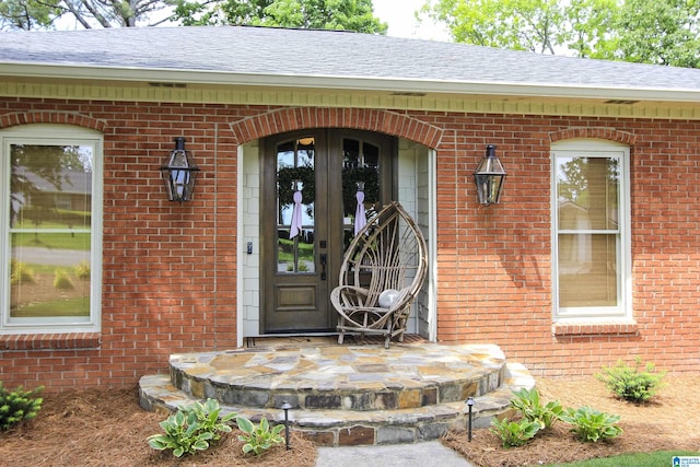 doorway to property with brick siding, a shingled roof, and french doors