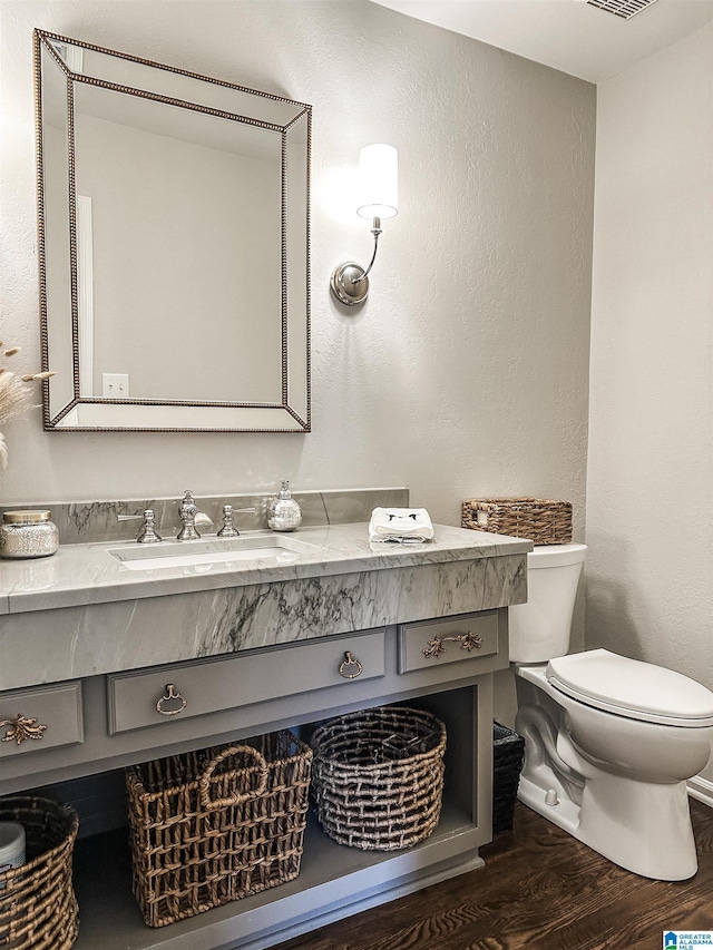 half bathroom with vanity, wood finished floors, visible vents, and toilet
