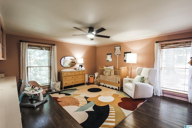 bedroom featuring crown molding, ceiling fan, a crib, visible vents, and hardwood / wood-style flooring