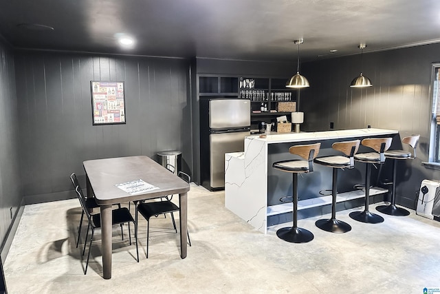 kitchen with freestanding refrigerator, a kitchen bar, light countertops, concrete floors, and hanging light fixtures
