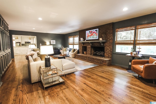living area featuring plenty of natural light, a brick fireplace, recessed lighting, and wood finished floors