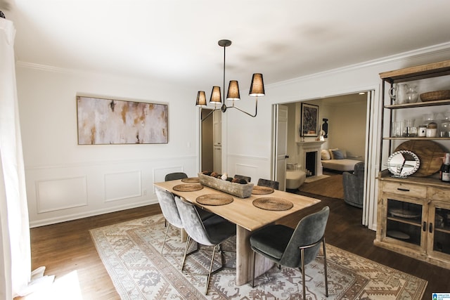 dining area featuring crown molding, a wainscoted wall, a fireplace, and dark wood finished floors