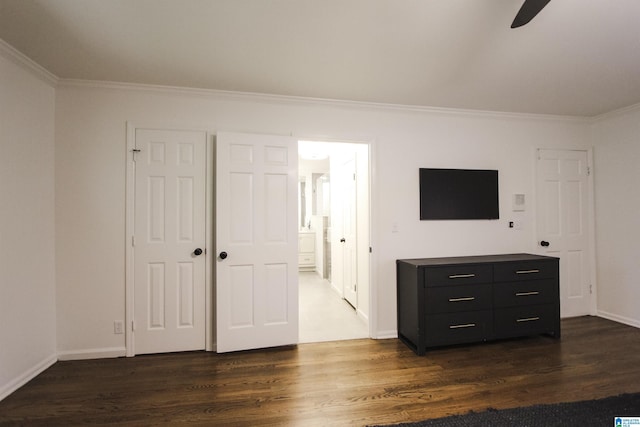 unfurnished bedroom with connected bathroom, dark wood-style flooring, baseboards, and ornamental molding