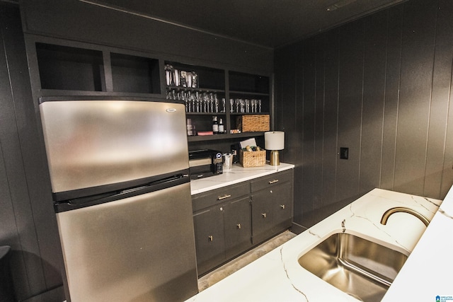 kitchen with open shelves, black microwave, light stone counters, a sink, and freestanding refrigerator