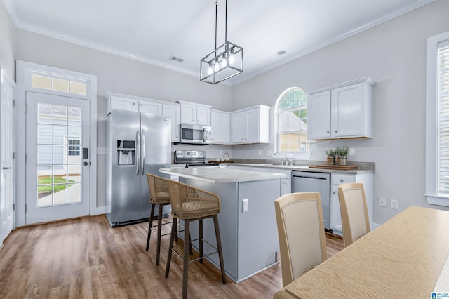kitchen featuring white cabinets, a breakfast bar, a center island, stainless steel appliances, and wood finished floors