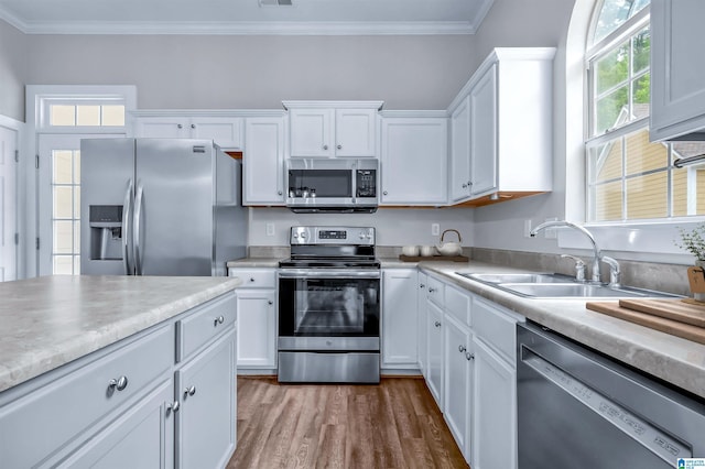 kitchen with a sink, stainless steel appliances, white cabinetry, and wood finished floors