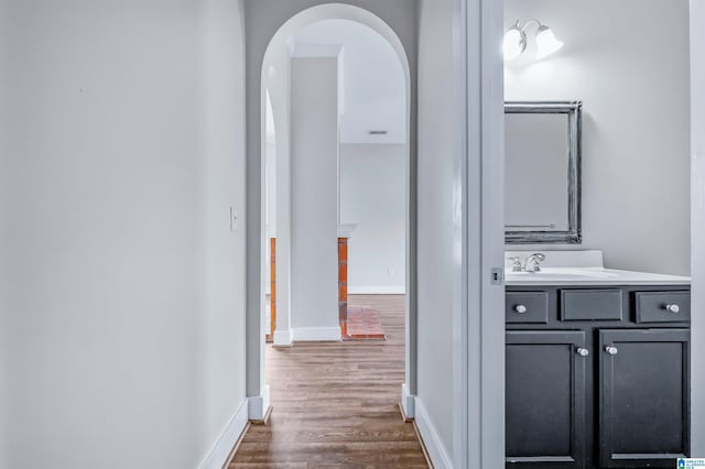 hall with dark wood-style flooring, arched walkways, baseboards, and a sink