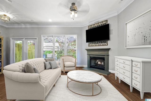 living area with a ceiling fan, crown molding, wood finished floors, baseboards, and a warm lit fireplace