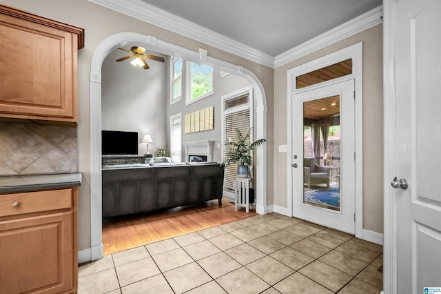 interior space with light tile patterned flooring, ceiling fan, a fireplace, baseboards, and ornamental molding