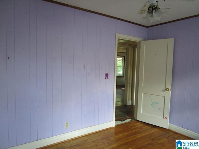 spare room featuring baseboards, wood walls, ornamental molding, and wood finished floors