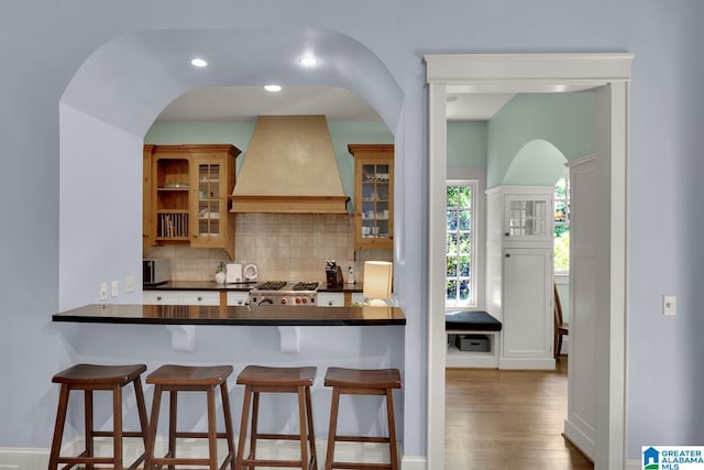 364 Stone Brook Cir, Hoover, AL 35226 - kitchen with a kitchen breakfast bar, backsplash, dark countertops, arched walkways, and custom exhaust hood