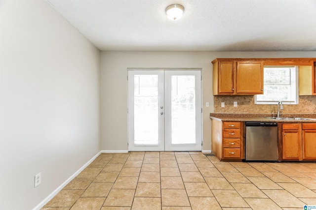 kitchen with french doors, tasteful backsplash, stainless steel dishwasher, brown cabinets, and a sink