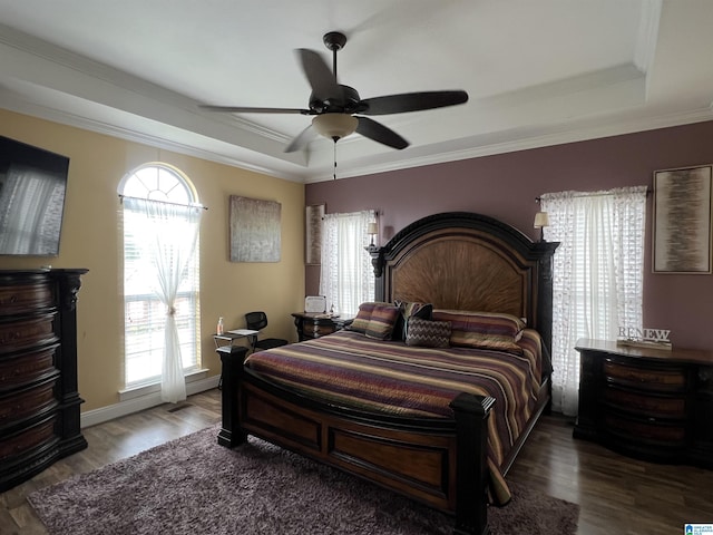 bedroom with ornamental molding, ceiling fan, wood finished floors, and a tray ceiling