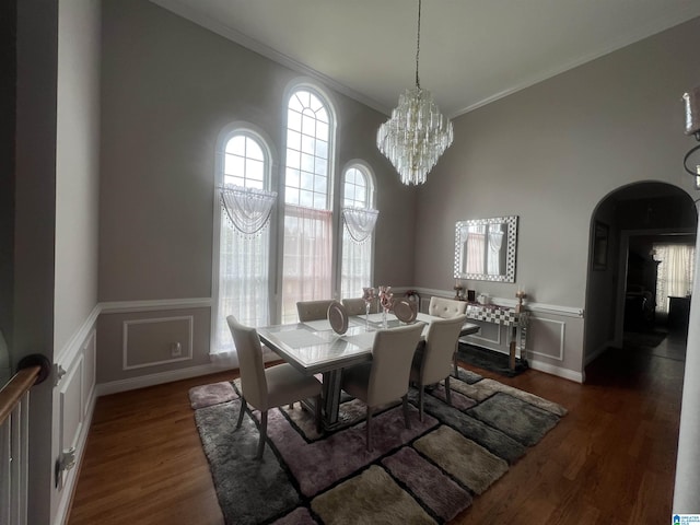 dining area featuring crown molding, arched walkways, a decorative wall, and dark wood-style floors