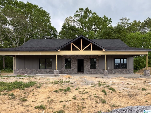 property under construction with board and batten siding, a shingled roof, and stone siding