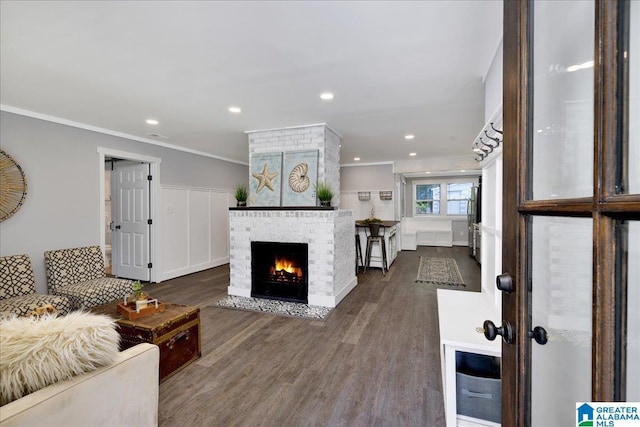 living room featuring a brick fireplace, recessed lighting, ornamental molding, and wood finished floors
