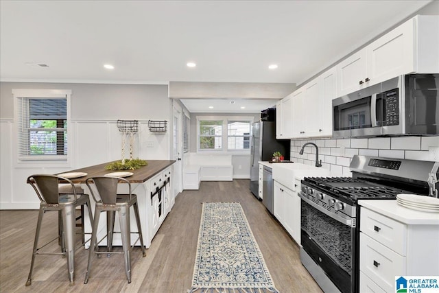 kitchen featuring decorative backsplash, appliances with stainless steel finishes, wood finished floors, a sink, and white cabinets