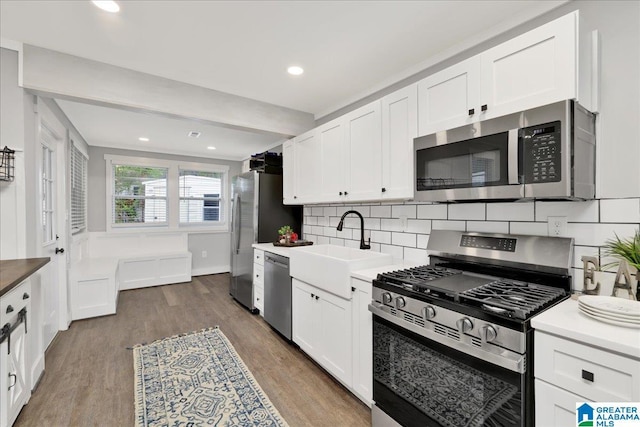 kitchen featuring decorative backsplash, wood finished floors, white cabinets, a sink, and appliances with stainless steel finishes