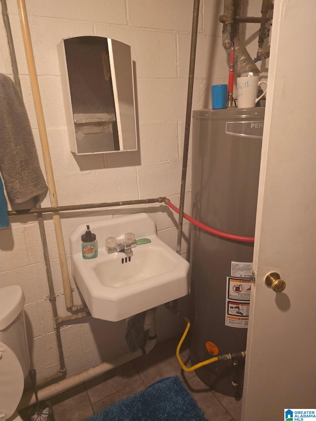 bathroom featuring concrete block wall, gas water heater, toilet, and a sink
