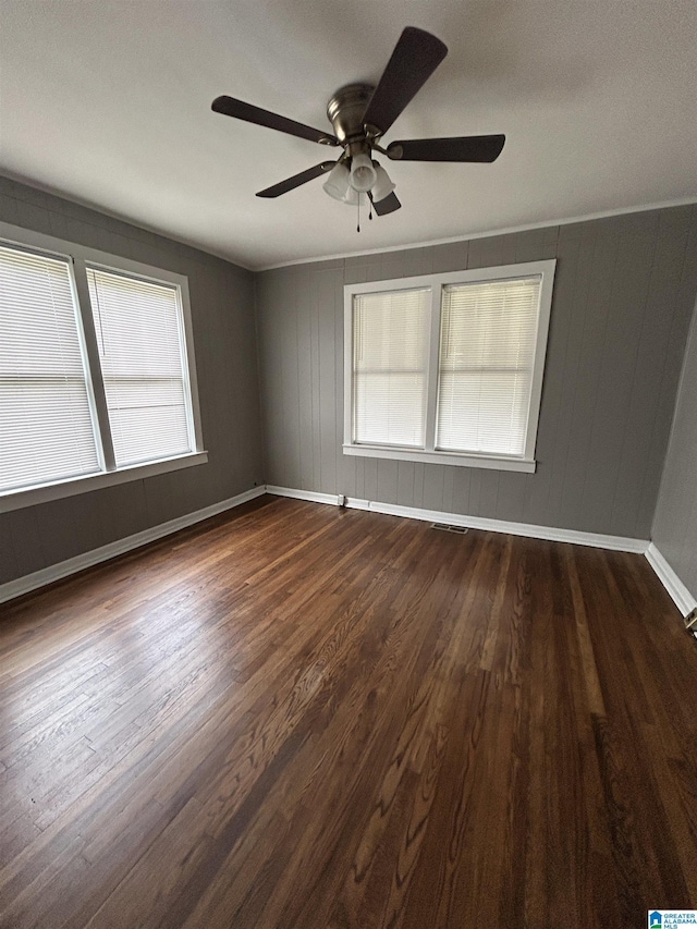 empty room with baseboards, visible vents, a ceiling fan, and dark wood-type flooring