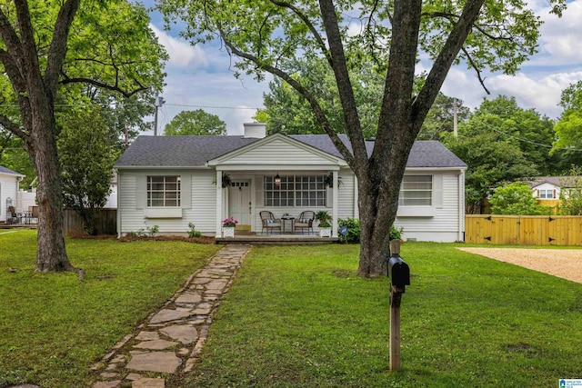 bungalow featuring covered porch, fence, and a front lawn