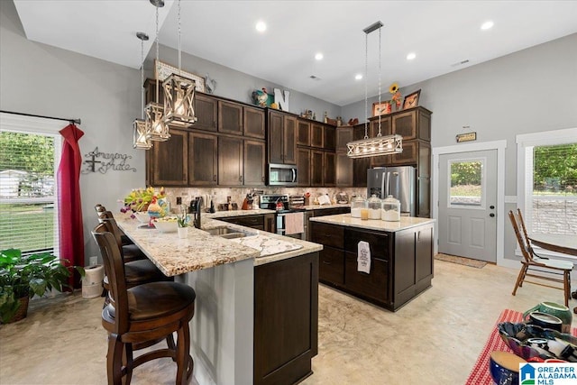 kitchen with light stone countertops, dark brown cabinetry, appliances with stainless steel finishes, a sink, and tasteful backsplash